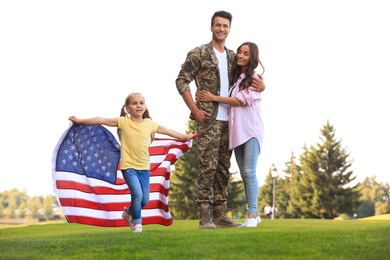 Photo of Little girl running with American flag, her father in military uniform and mother at sunny park