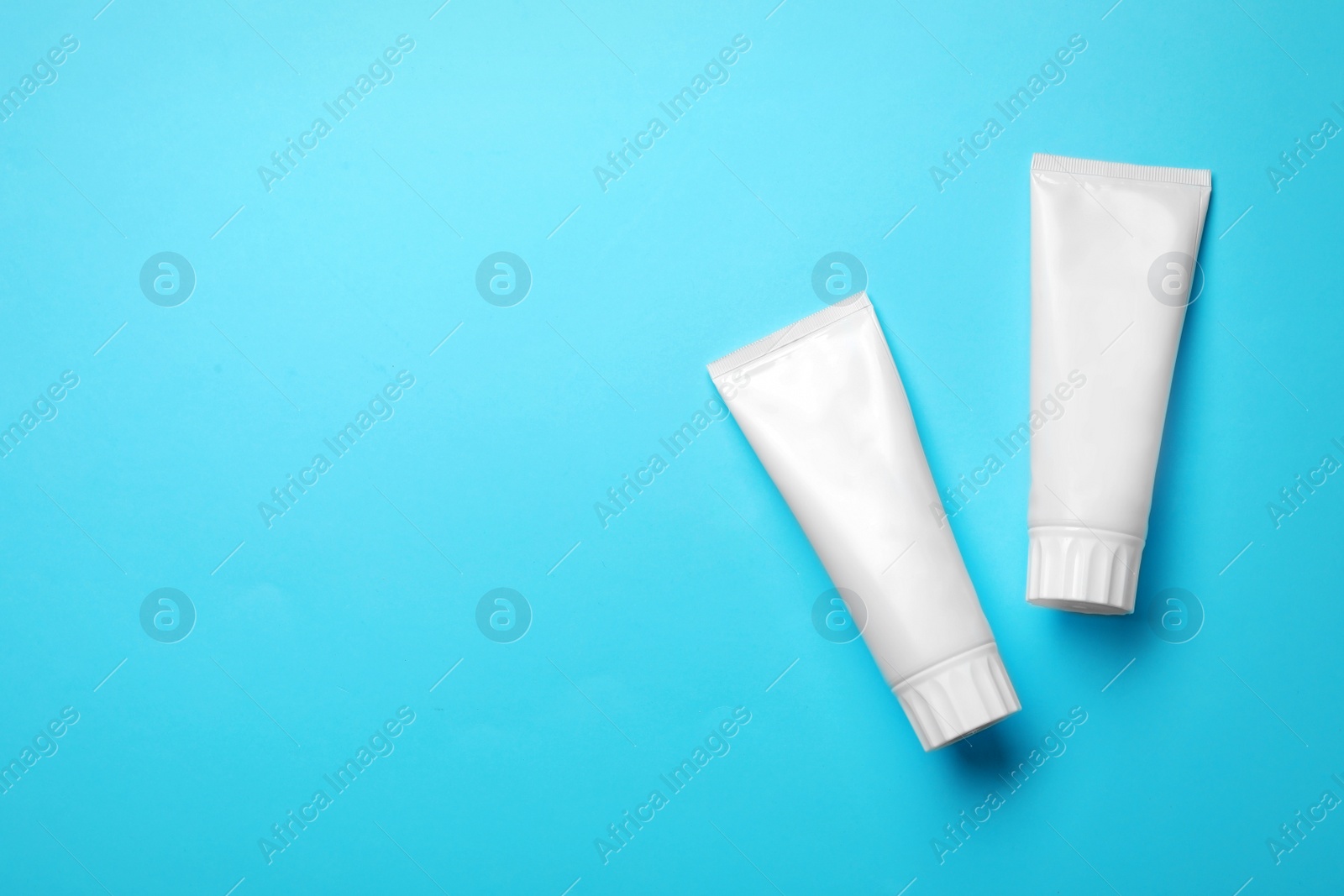 Photo of Blank tubes of toothpaste on color background, top view with space for text