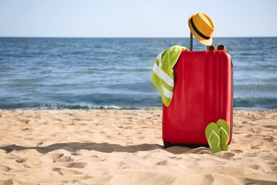 Bright suitcase and different beach accessories on sand near sea. Space for text