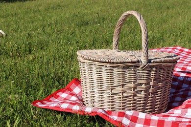 Photo of Picnic basket with checkered tablecloth on green grass outdoors, space for text