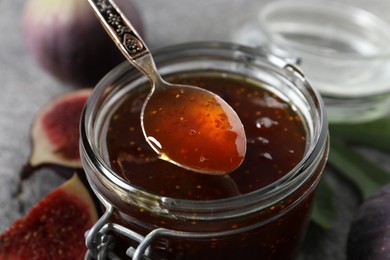 Photo of Spoon with tasty sweet jam over jar and fresh figs on table, closeup