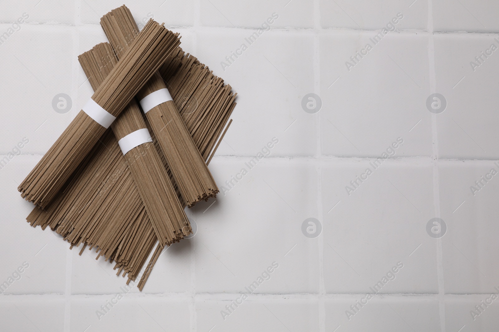 Photo of Uncooked buckwheat noodles (soba) on white tiled table, top view. Space for text