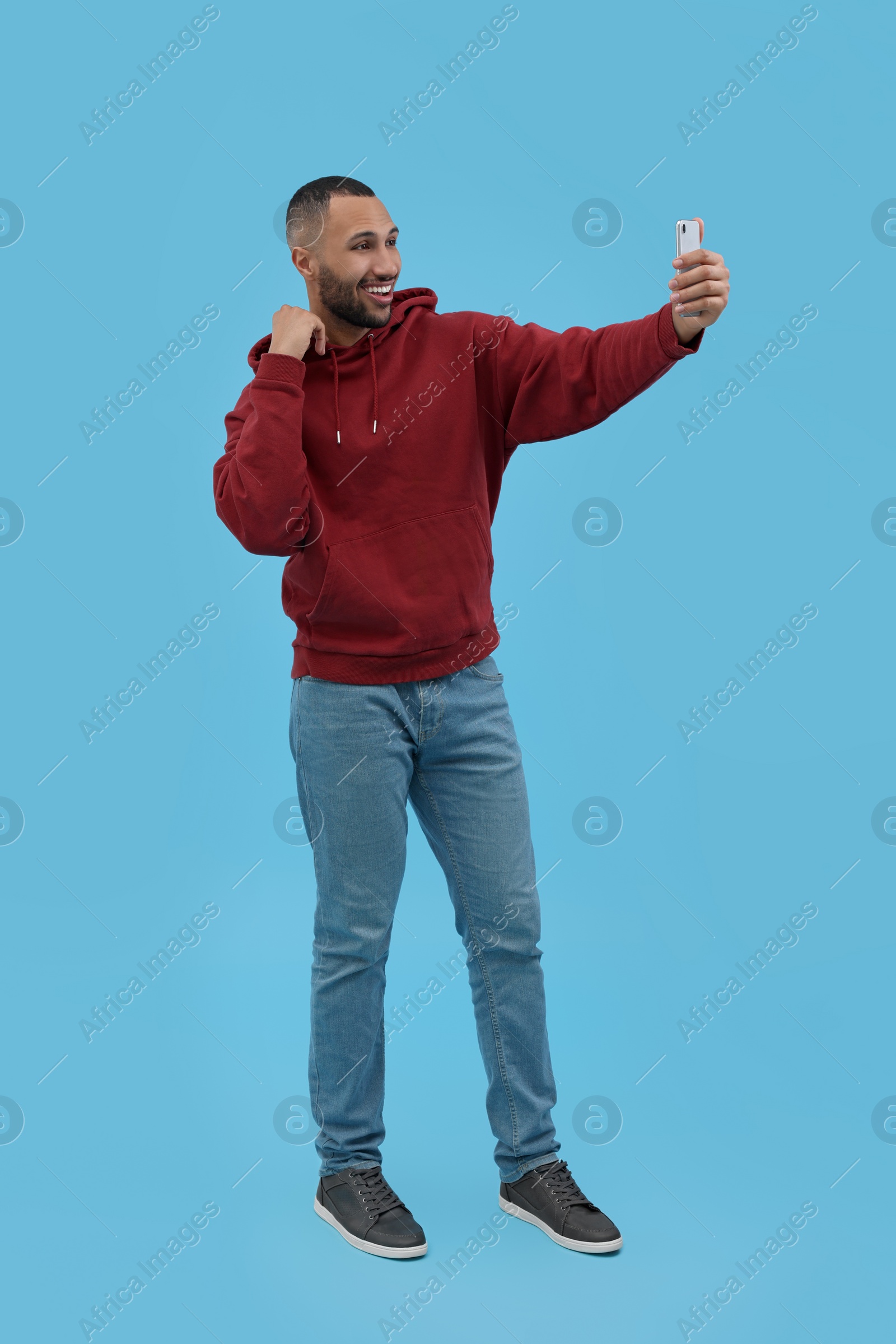 Photo of Smiling young man taking selfie with smartphone on light blue background