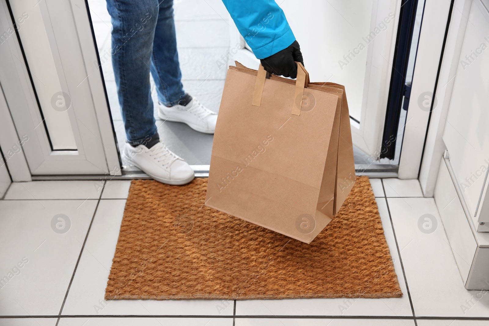 Photo of Courier bring paper bags with takeaway food to doorway, closeup. Delivery service during quarantine due Covid-19 outbreak