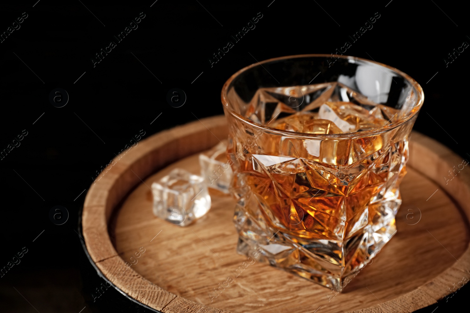 Photo of Golden whiskey in glass with ice cubes on wooden barrel. Space for text