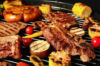 Photo of Fresh grilled meat steaks and vegetables on barbecue grate, closeup