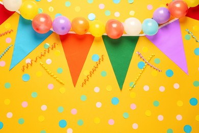 Bunting with colorful triangular flags and other festive decor on yellow background, flat lay