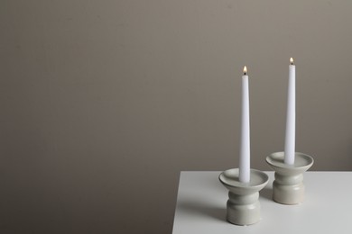Holders with burning candles on white table near pale brown wall, space for text