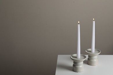 Photo of Holders with burning candles on white table near pale brown wall, space for text