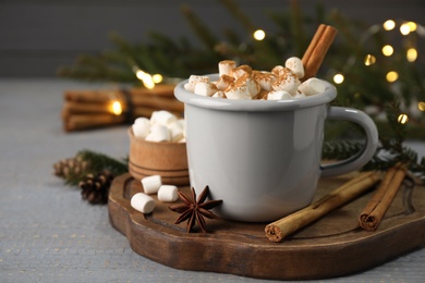 Cup of hot drink with aromatic cinnamon and marshmallows on grey wooden table against blurred lights