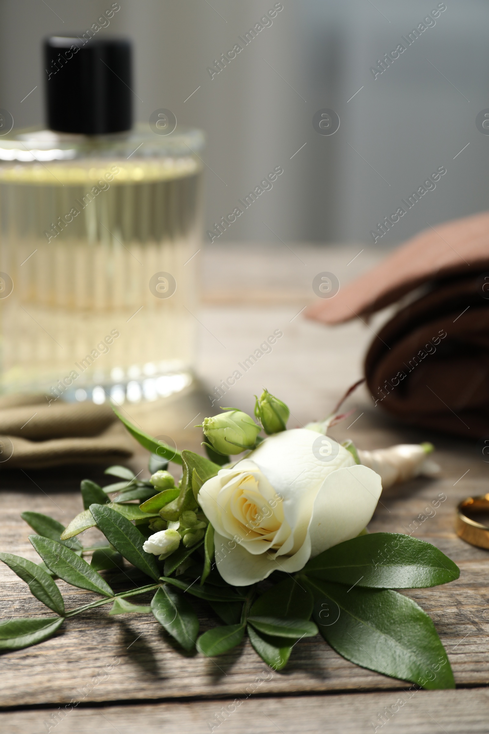 Photo of Wedding stuff. Stylish boutonniere, perfume and ring on wooden table, closeup