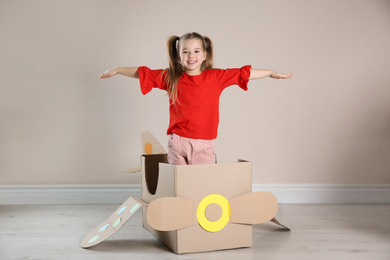 Photo of Cute little child playing with cardboard plane near beige wall