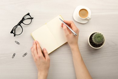 Photo of Woman writing in notebook at light wooden table, top view