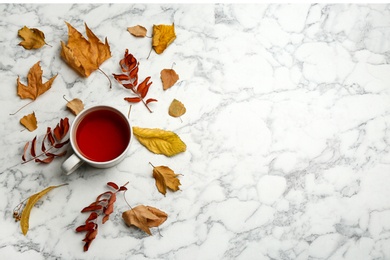 Flat lay composition with cup of hot drink and autumn leaves on white marble background, space for text. Cozy atmosphere