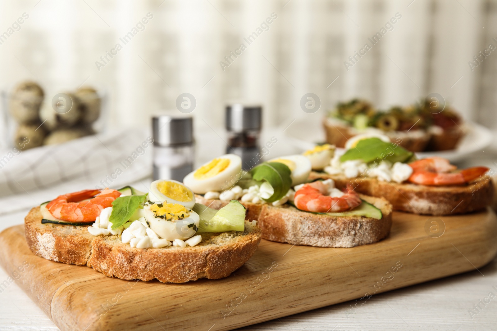 Photo of Cutting board of delicious bruschettas with shrimps on kitchen table