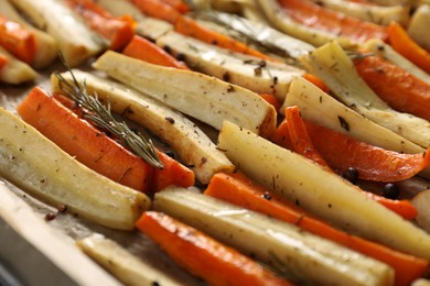 Photo of Delicious baked parsnips and carrots with rosemary on baking tray, closeup