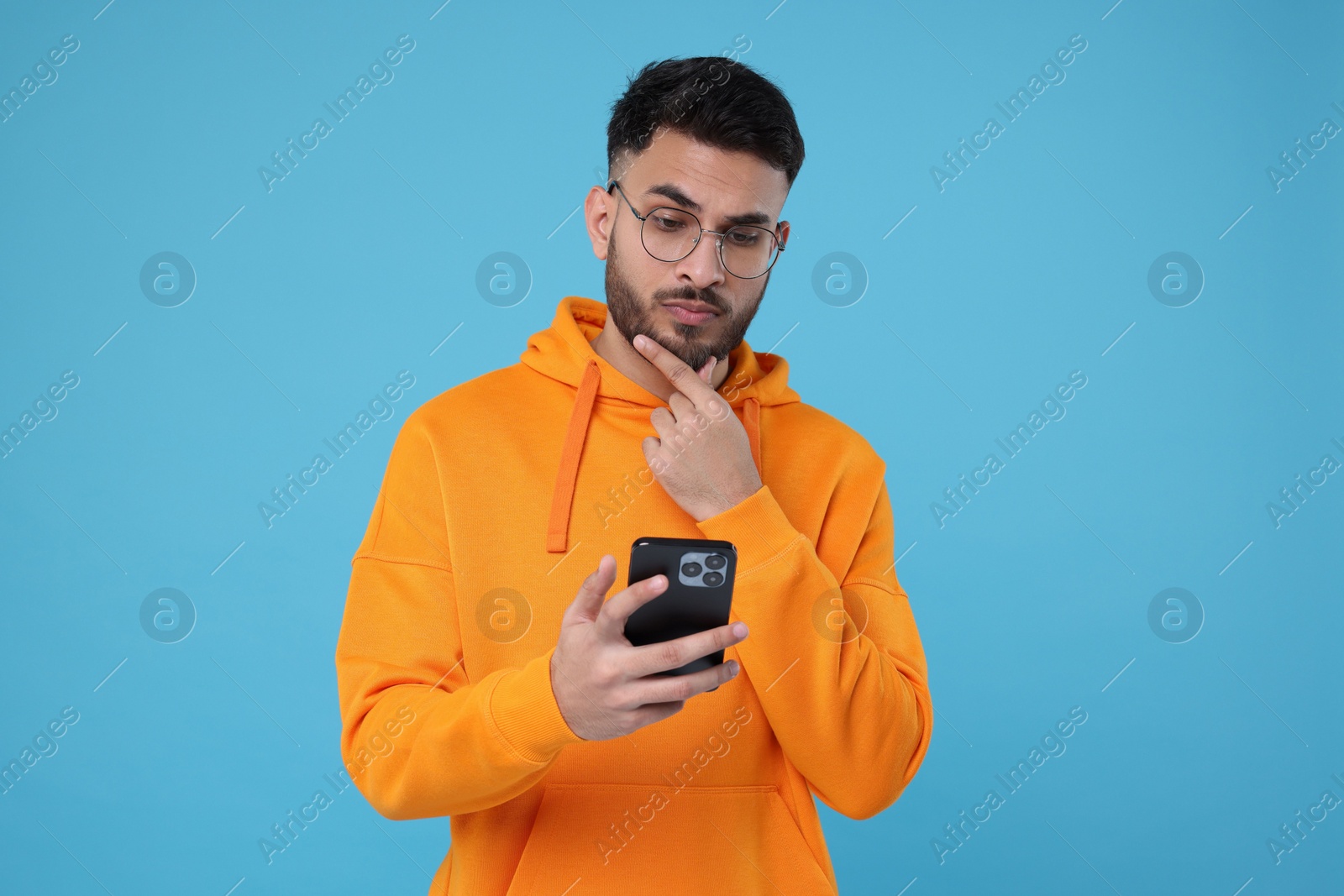 Photo of Handsome young man using smartphone on light blue background