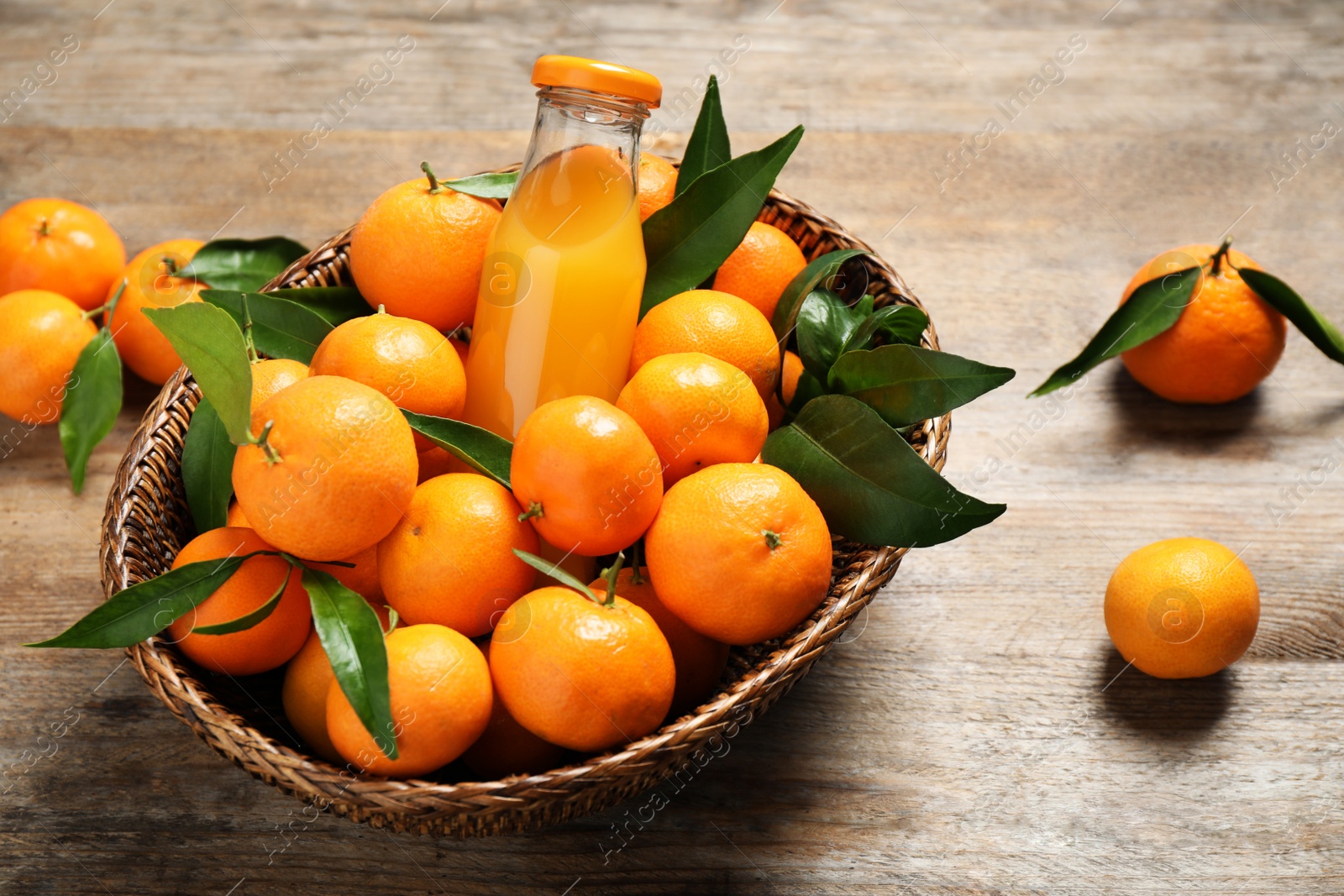 Photo of Basket with fresh tangerines and bottle of juice on wooden table