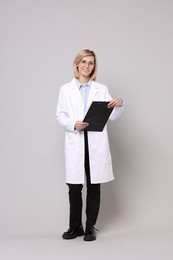 Smiling doctor with clipboard on grey background