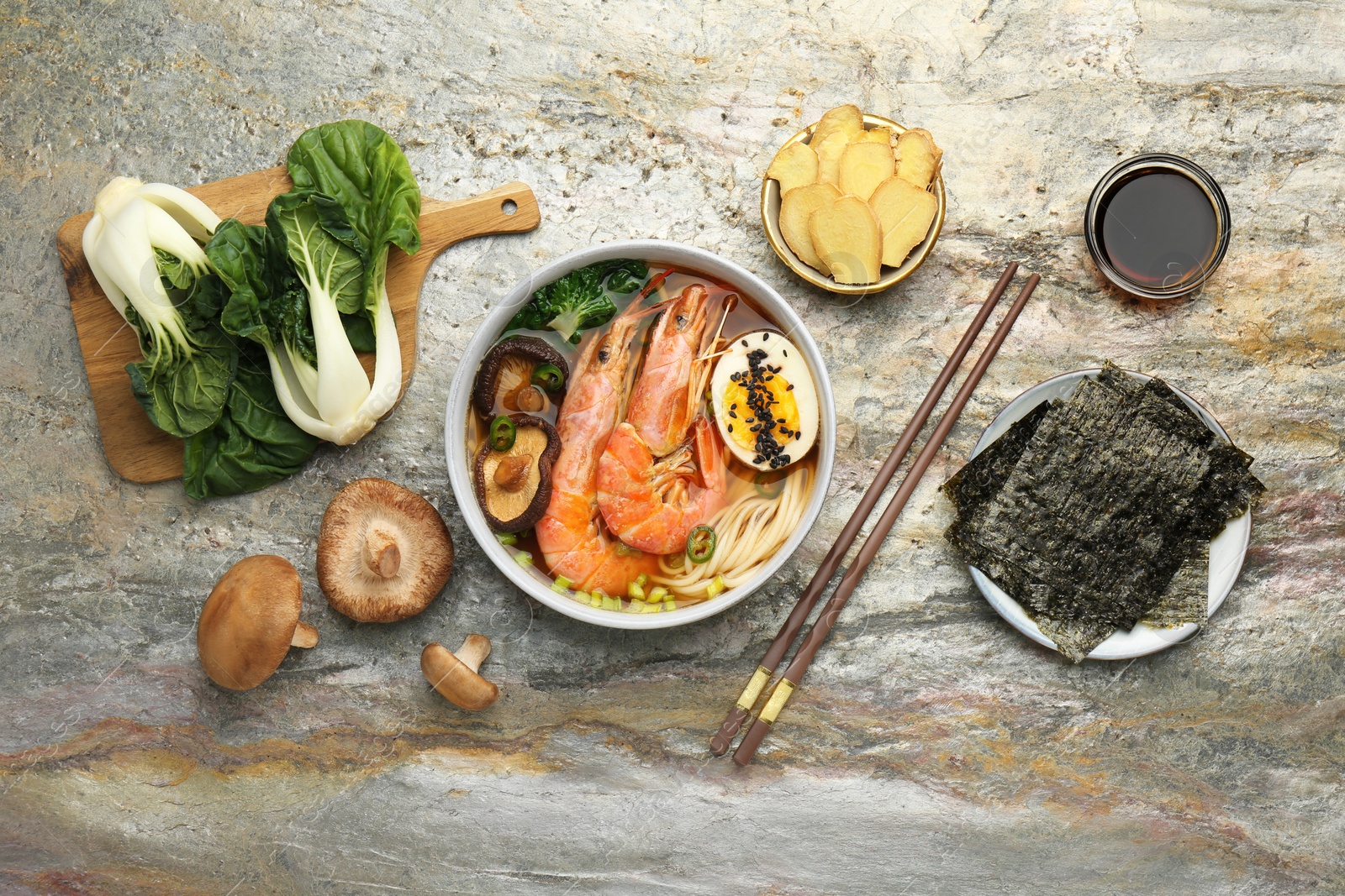 Photo of Delicious ramen with shrimps, ingredients and chopsticks on grey textured table, flat lay. Noodle soup