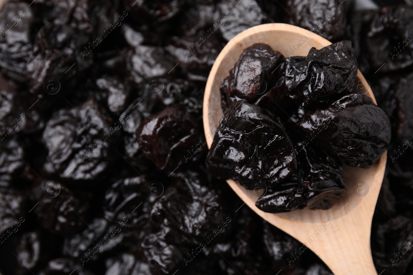 Photo of Pile of sweet dried prunes and spoon, top view. Space for text