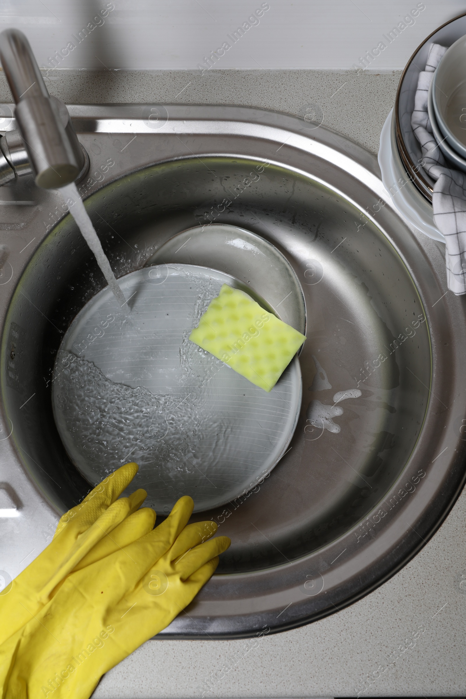 Photo of Washing plates, sponge and rubber gloves in kitchen sink, above view