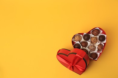 Photo of Heart shaped box with delicious chocolate candies on yellow background, flat lay. Space for text