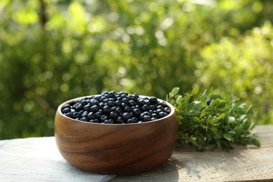Photo of Delicious bilberries in bowl on wooden table outdoors