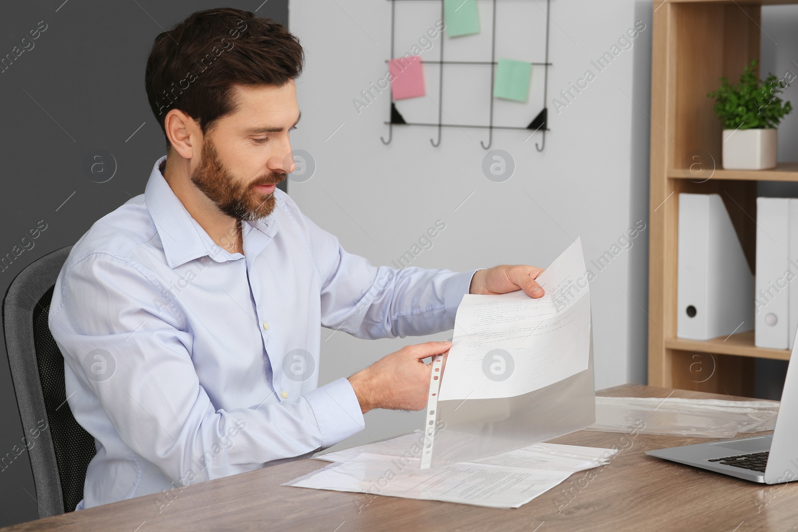 Photo of Businessman putting document into punched pocket at wooden table in office