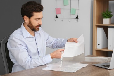 Businessman putting document into punched pocket at wooden table in office
