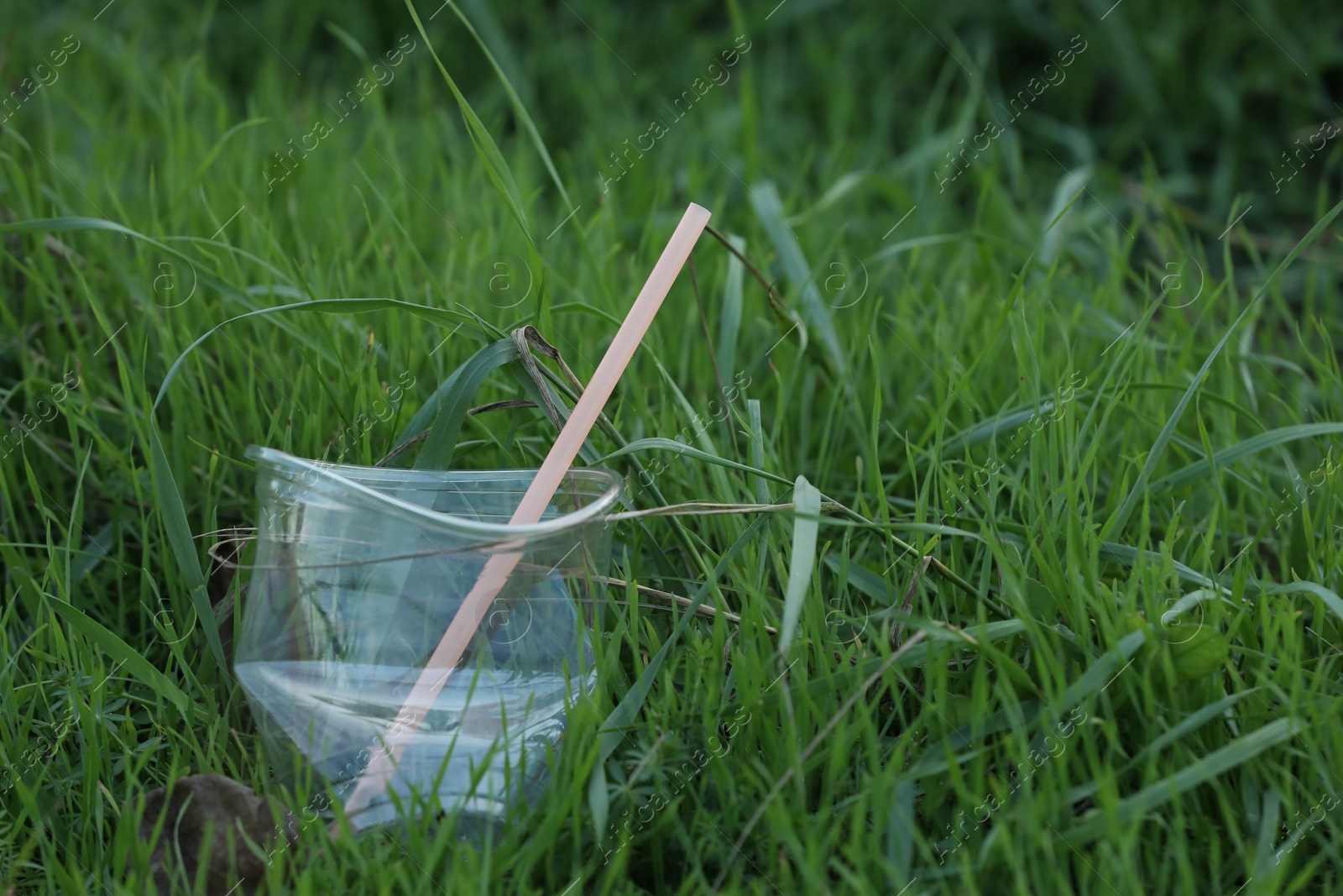 Photo of Used plastic cup with straw on grass outdoors, space for text. Environmental pollution concept