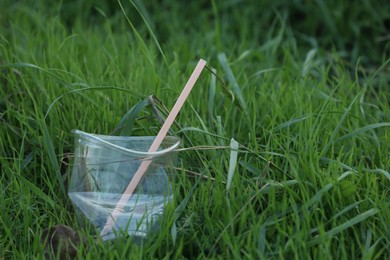 Photo of Used plastic cup with straw on grass outdoors, space for text. Environmental pollution concept