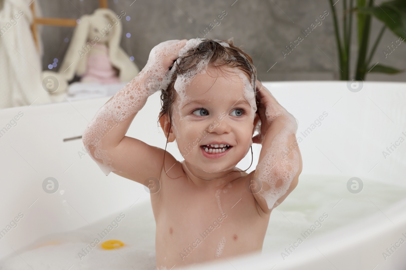 Photo of Cute little girl washing hair with shampoo in bathroom