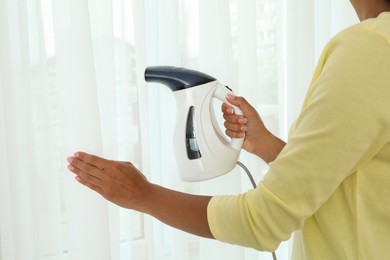 Woman steaming curtain near window at home, closeup