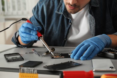 Photo of Technician repairing broken smartphone at table, closeup