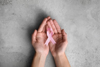 Photo of Woman holding pink ribbon at grey table, top view. Breast cancer awareness concept