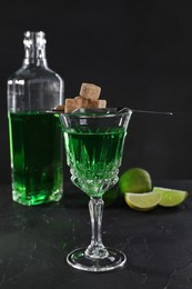 Photo of Absinthe in glass, brown sugar and lime on black table. Alcoholic drink