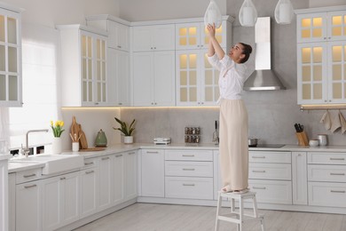 Photo of Woman on ladder changing lightbulb in ceiling lamp at home