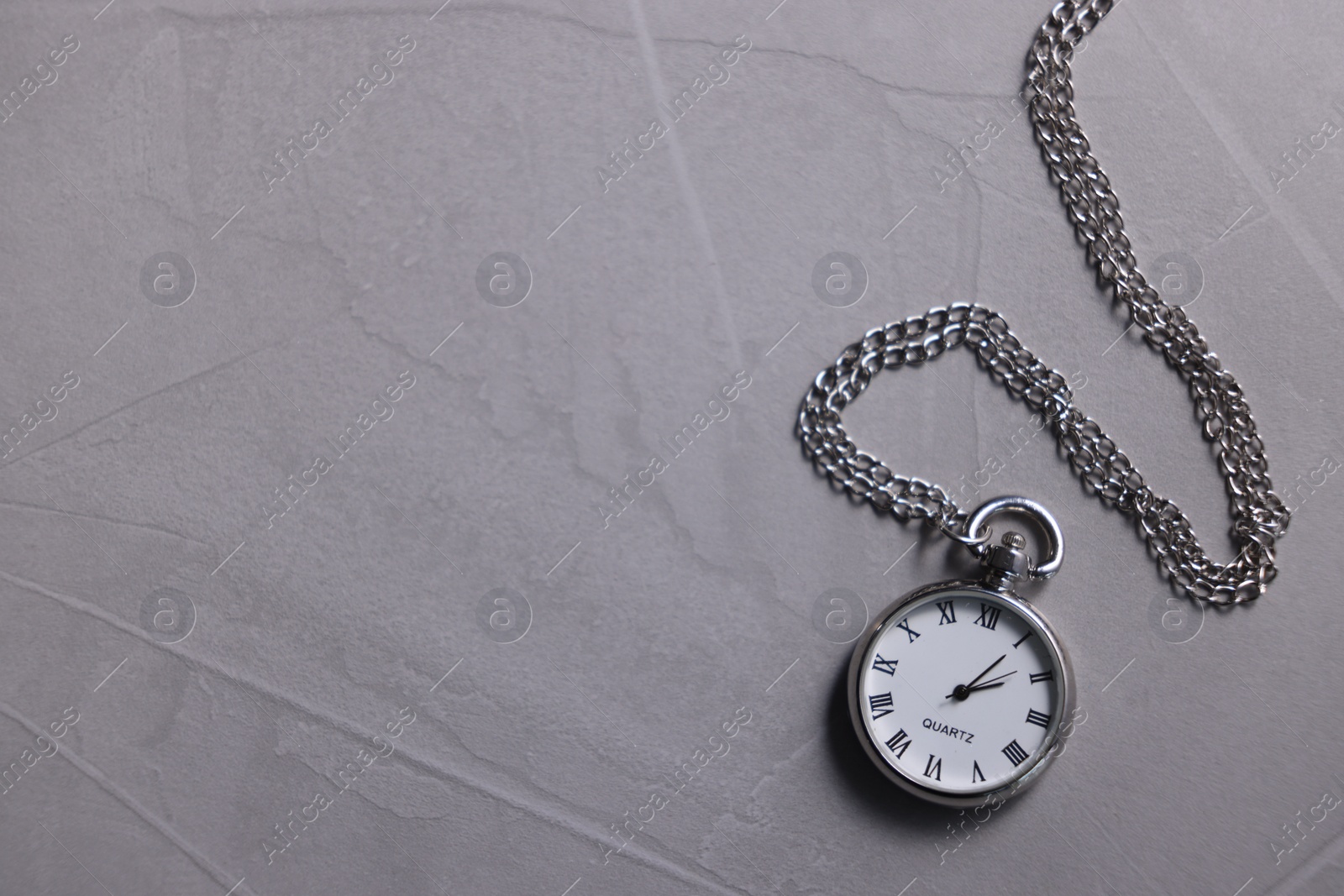 Photo of Silver pocket clock with chain on grey textured table, top view. Space for text