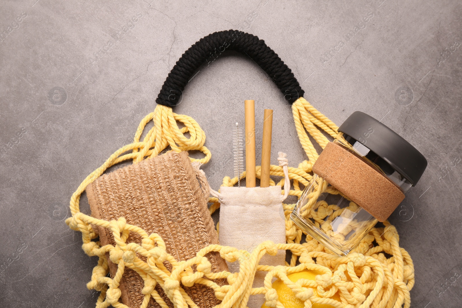 Photo of Fishnet bag with different items on grey table, top view. Conscious consumption