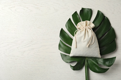 Photo of Cotton eco bag and monstera leaf on white wooden table, top view. Space for text