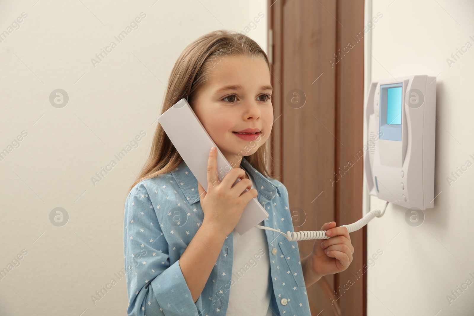 Photo of Cute little girl answering intercom call indoors