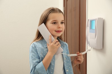 Photo of Cute little girl answering intercom call indoors