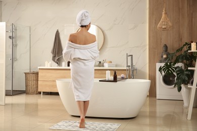 Photo of Young woman near tub in bathroom, back view