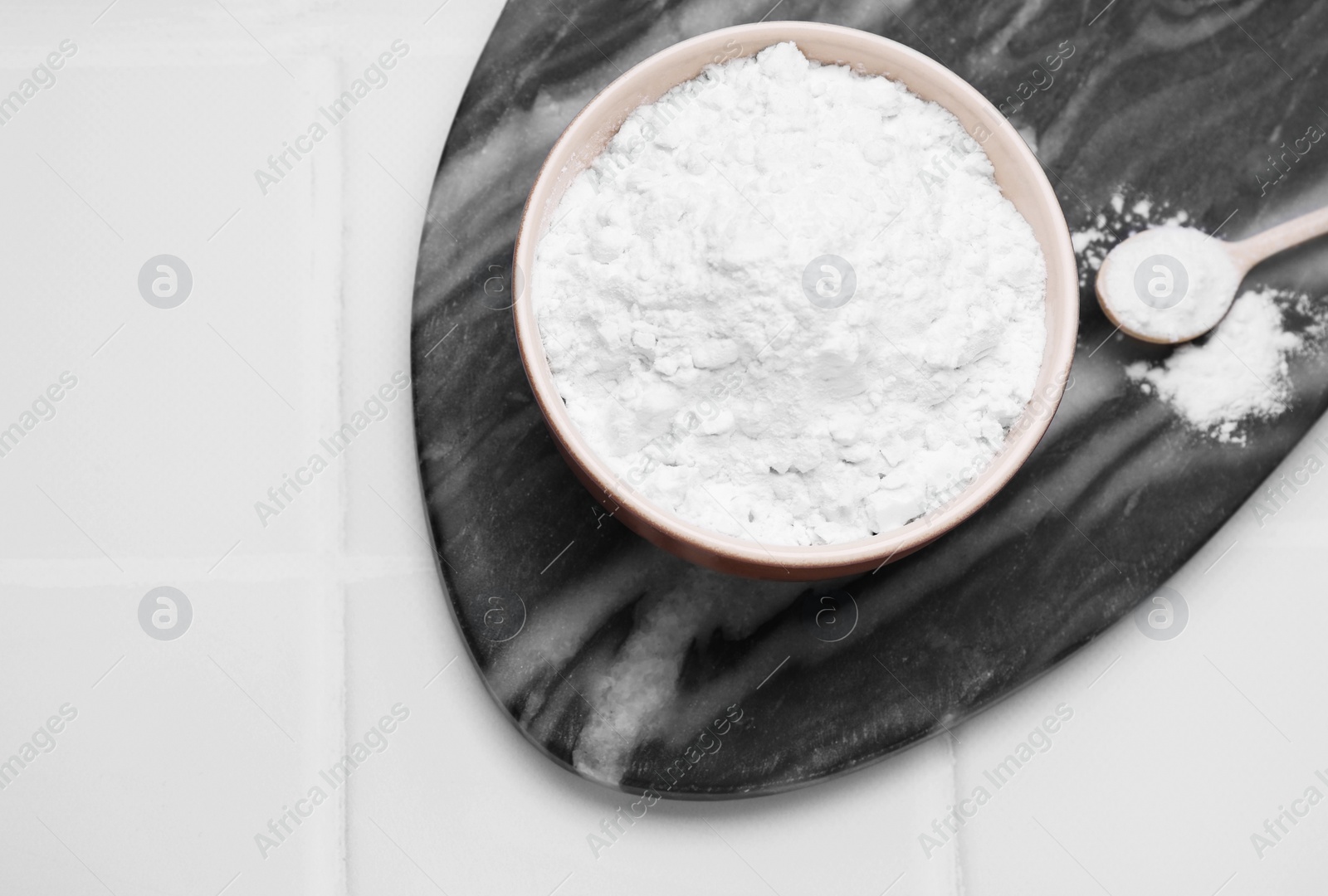 Photo of Bowl and spoon of natural starch on white tiled table, top view. Space for text