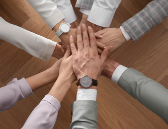 Photo of People holding hands together over wooden background, top view. Unity concept