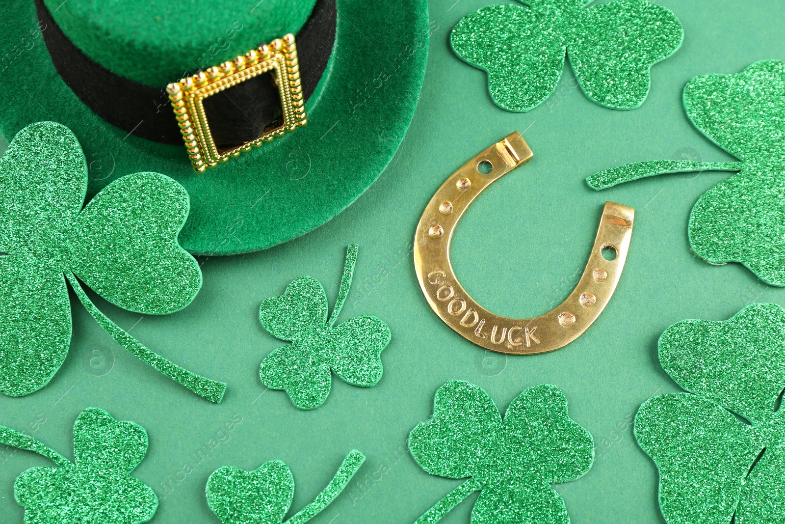 Photo of St. Patrick's day. Leprechaun hat, golden horseshoe and decorative clover leaves on green background, above view