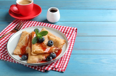 Photo of Delicious crepes served with blueberries, mint, syrup and cup of coffee on blue wooden table. Space for text