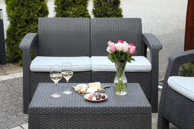 Photo of Vase with roses, glasses of wine and food on rattan table on outdoor terrace