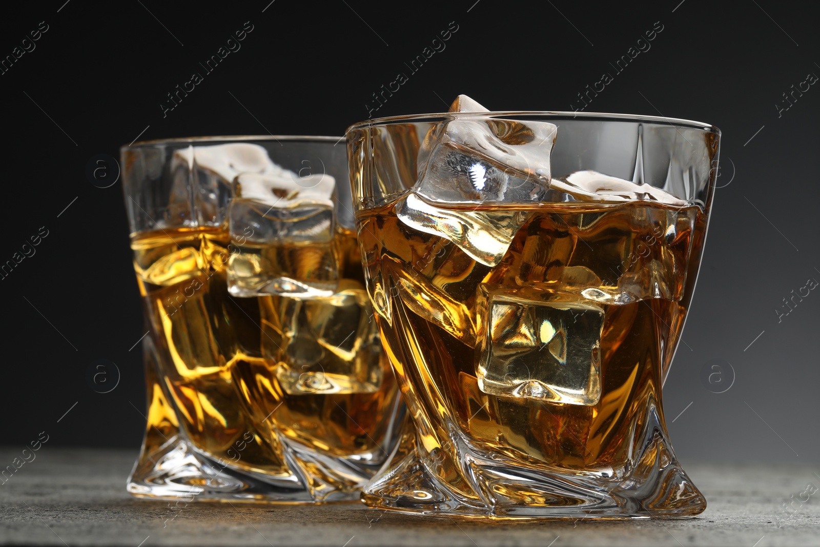 Photo of Whiskey and ice cubes in glasses on grey textured table, closeup